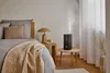 A humidifier is shown in a bedroom setting on a side table next to a bed. Náhľad obrázku produktu