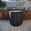 A round table covered with a black protective cover sits on a paved patio surrounded by plants and outdoor furniture. Anteprima dell’immagine prodotto