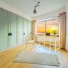 A room with a desk, chair, and large closet, with a sunset visible through the window. Podgląd zdjęcia produktu