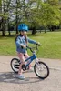 A young girl wearing a blue helmet and denim jacket rides a blue bicycle in a park. Voir les images du produit