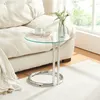 A glass-top side table next to a sofa, with a book and cup on the table and a vase with greenery. Produktbild-Vorschau
