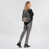 A woman wearing a black sweater and gray jeans stands with her back to the camera, wearing a backpack. Voir les images du produit
