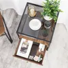 A bedside table with an open drawer, displaying various items, placed on a carpeted floor next to a chair. Produktbild-Vorschau