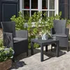 A patio set with two chairs and a table on a paved patio, with greenery and a building in the background. Produktbild-Vorschau