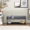 A bench with a shoe rack underneath, placed in an entryway or hallway with stairs and artwork on the wall. Produktbild-Vorschau
