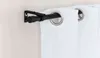 A close-up view of a black adjustable curtain rod mounted on a wall, with white curtains hanging from it. Produktbild-Vorschau