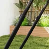 Close-up view of black poles, likely part of a sports rebounder, set against a backdrop of green grass, a wooden planter box, and bamboo fencing with palm fronds. Voir les images du produit