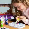 A young girl is using a set of colorful gel pens to create art on a white tray. Produktbild-Vorschau