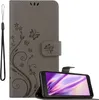 A grey flip phone case with a floral and butterfly design is shown open, with a smartphone inside. A black wrist strap is attached to the left side of the case. Náhľad obrázku produktu