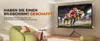 A living room scene with a projector displaying a sports game on a screen, with a comfortable chair and a small table with the projector on it. Produktbild-Vorschau