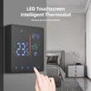 A digital thermostat is mounted on a gray wall in a bedroom setting, with a bed and nightstand visible in the background. A hand is shown interacting with the thermostat's touchscreen. Produktbild-Vorschau