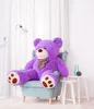 A large purple teddy bear is sitting in a light blue armchair in a room with white curtains and a white wall. Produktbild-Vorschau