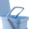 A close-up view of the top of a light blue plastic trash can with its lid open and a gray handle. Produktbild-Vorschau