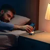 A man in bed reaches for a wireless charging stand on his nightstand. Produktbild-Vorschau