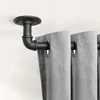 A close-up view of a black pipe-style curtain rod mounted to a ceiling, holding up gray curtains. Produktbild-Vorschau