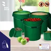 Several green buckets filled with different items, including liquid, grain, and tomatoes, are displayed on a table. Apples and a smaller green container with brown pellets are also visible. The background shows a window and a hint of a room. Podgląd zdjęcia produktu