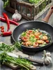 A frying pan with shrimp and vegetables being cooked, surrounded by fresh ingredients like chili peppers, garlic, and parsley on a wooden table. Voir les images du produit