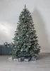 A decorated Christmas tree with presents underneath and a trunk to the side, set against a white paneled wall. Produktbild-Vorschau