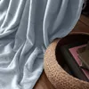 A light blue blanket is draped over a wooden floor, next to a woven basket filled with books. Produktbild-Vorschau