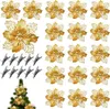 A collection of gold glitter poinsettia decorations and clips arranged on a white background, with a small section of a decorated Christmas tree in the bottom left corner. Produktbild-Vorschau