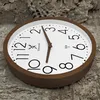A wooden wall clock is placed on a textured, bark-like surface. Voir les images du produit