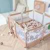 A baby playpen filled with balls is set up next to a bed in a nursery. Anteprima dell’immagine prodotto