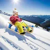 A child sledding down a snowy mountain with a scenic view of a lake and mountains in the background. Voir les images du produit