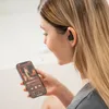 A woman is holding a smartphone and wearing wireless earphones. Produktbild-Vorschau