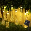 Solar-powered string lights with teardrop-shaped LED bulbs are displayed outdoors, attached to a fence and draped over grass and foliage. Produktbild-Vorschau