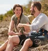 A couple is sitting on rocks outdoors, with one person holding a flask. Podgląd zdjęcia produktu