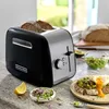 A black and silver KitchenAid toaster with bread inside, on a granite countertop with various breakfast items. Voir les images du produit