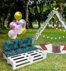 A picnic setup in a garden with a pallet sofa, cushions, balloons, and a teepee. Produktbild-Vorschau