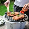 A person is grilling steaks and tomatoes on a portable electric grill outdoors. Produktbild-Vorschau