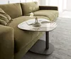 A modern living room scene featuring a green sectional sofa and a small, uniquely shaped side table with a marble-like top. Produktbild-Vorschau