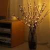 A vase of illuminated branches sits on a table next to a shelf unit. Náhled obrázku produktu