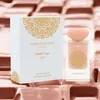A perfume bottle and its box are displayed on a textured pink and brown surface. Voir les images du produit