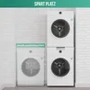 Two white washing machines stacked on top of each other, with a smaller washing machine outlined to the left, indicating space-saving. The background is a white brick wall. Voir les images du produit
