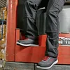 A person wearing black work pants and grey and red work shoes is sitting on the step of a red forklift in a warehouse. Podgląd zdjęcia produktu