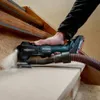 A person is using a Metabo multitool to sand a wooden surface, likely stairs, with a vacuum hose attached for dust collection. Náhľad obrázku produktu