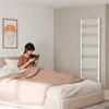 A woman is reading a book in bed, with a white towel radiator in the background. Produktbild-Vorschau