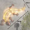 A decorative gecko-shaped solar light mounted on a wall, with bamboo-like plants in the foreground. Produktbild-Vorschau
