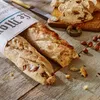 Two baguettes wrapped in newspaper, with biscotti and hazelnuts on a wooden table. Anteprima dell’immagine prodotto