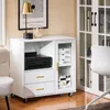 A white sideboard with drawers and a glass-fronted cabinet, placed on a wooden floor next to a chair and a larger cabinet. Produktbild-Vorschau