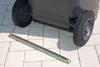 A close-up shot of a garbage bin's wheels and a metal rod on a paved surface. Anteprima dell’immagine prodotto
