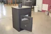 A black wood-burning stove with its door ajar, displayed indoors in what appears to be a showroom or warehouse. Produktbild-Vorschau