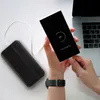 A person is charging a smartphone with a power bank, with a laptop in the background. Produktbild-Vorschau