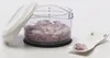 A clear shot of a manual food chopper filled with chopped red onions, with its lid propped open and a small spoon with a few onion pieces next to it. Produktbild-Vorschau