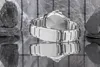 A silver watch with a metal band is shown on a reflective surface, with rocks in the background. Voir les images du produit