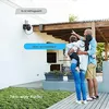 A family is standing on a patio, looking up at a security camera mounted on the wall. Speech bubbles indicate a conversation between the camera and the family. Produktbild-Vorschau