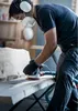A person is sanding a piece of wood with a power tool in a workshop. Produktbild-Vorschau
